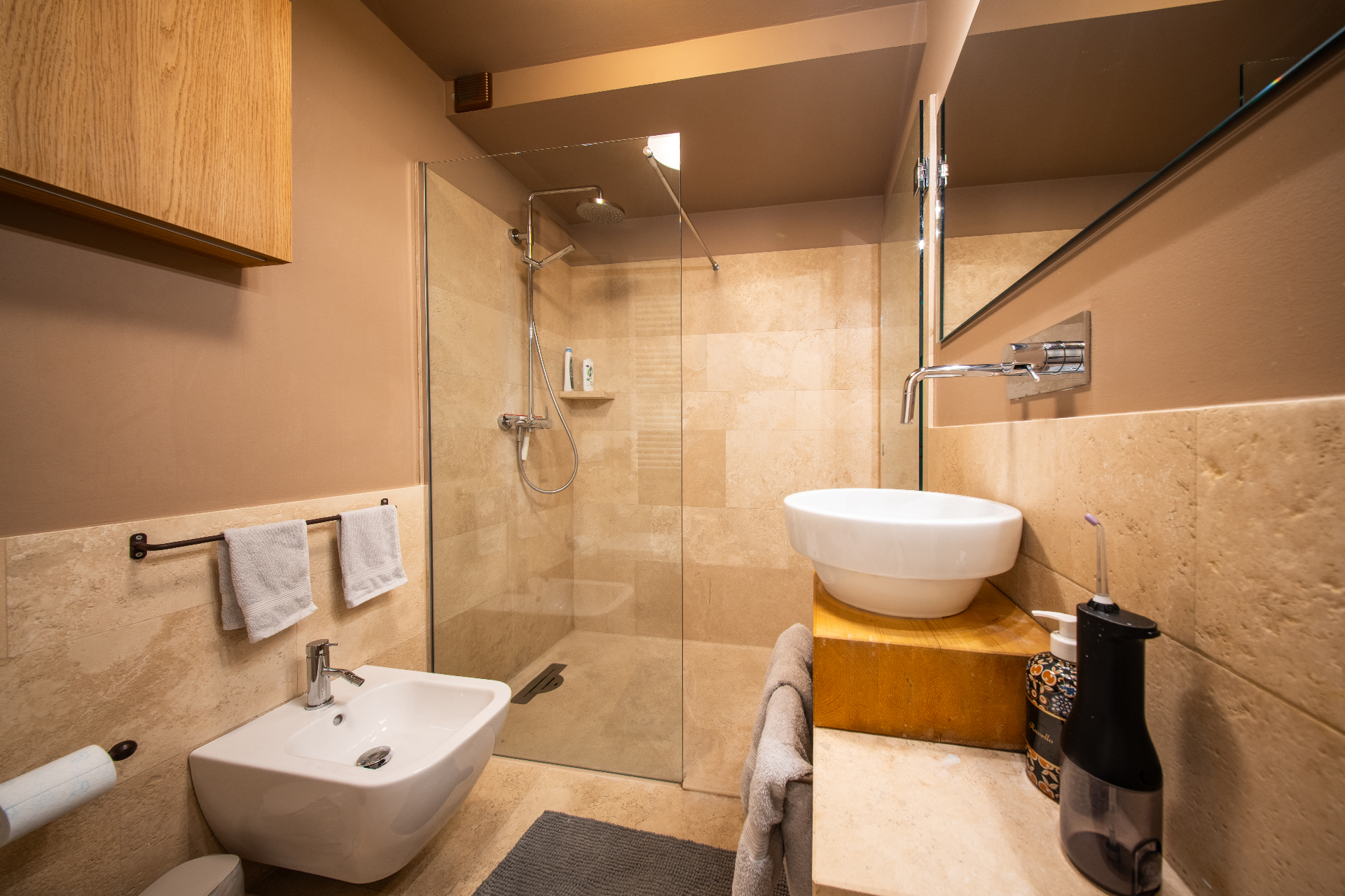 Travertine walk-in shower with vessel basin