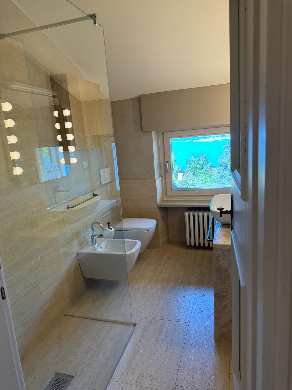 Travertine bathroom with a window framing Lake Garda
