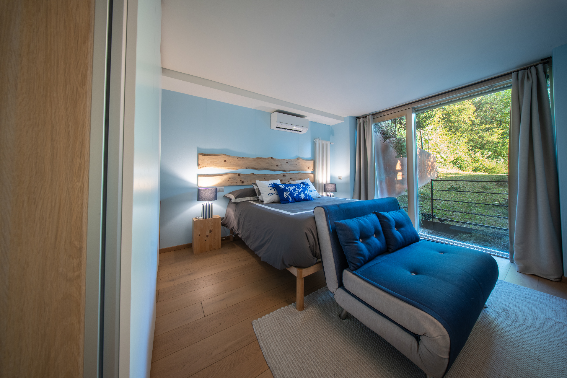 Blue bedroom with live-edge headboard and chaise looking to the garden